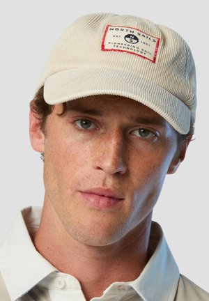 Cappello in velluto a coste color crema con una toppa quadrata rossa recante la scritta "NORTH SAILS" e "PIONEERING SAIL TECHNOLOGY". Design semplice e strutturato.