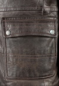 Donkerbruine leren jaszak met een flap die is vastgezet met twee zilveren drukknoopjes en zichtbare stikdetails.