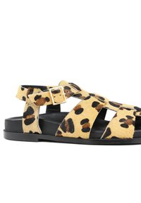 Sandalias de estampado de leopardo hechas de piel texturizada de color marrón claro con manchas negras. Cuenta con una correa ajustable y una suela plana negra.