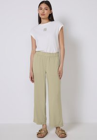 Lichtgroene wijdvallende broek met een elastische tailleband en twee voorzakken, gecombineerd met een witte t-shirt met korte mouwen met een kleine print.