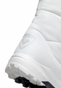 Bílé polstrované boty s texturovaným povrchem a gumovou podrážkou. Na boku mají vyvýšené, embosované logo. Hladké materiály po celém povrchu.