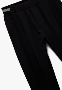 Schwarze Stretchhosen mit elastischem Bund, grauem Akzentstreifen, Seitentaschen und einer glatten, eleganten Textur.