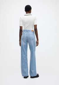 Λευκή ριμπ μπλούζα με κοντά μανίκια, συνδυασμένη με ανοιχτό μπλε τζιν παντελόνι φαρδιάς γραμμής με πίσω τσέπες και ταμπά δερμάτινη ετικέτα. Μαύρα παπούτσια με πάτο πλατφόρμα.