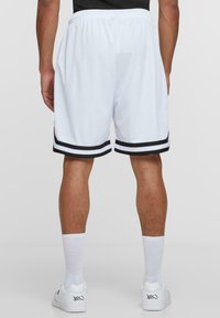 White athletic shorts with a perforated texture, featuring black striped accents at the hem, elastic waistband, and a relaxed fit.