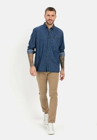 Denim skjorte med knapper i mørkeblå, med en brystlomme og lange ærmer, parret med lyse khaki bukser og hvide sneakers.