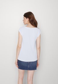 T-shirt branca de manga curta com um corte descontraído, decote redondo e textura suave, usada com uma saia mini de ganga escura.