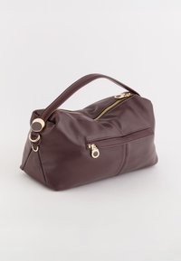 Burgundowa skórzana torba z górnym uchwytem, złotym zamkiem błyskawicznym i małą przednią kieszonką, charakteryzująca się gładką fakturą i zaokrąglonym kształtem.