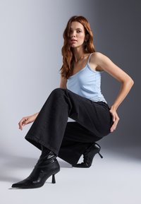 Lys blå cami med delikat blonderkant, parret med højtaljede sorte vide jeans og spidse sorte hæle støvler.