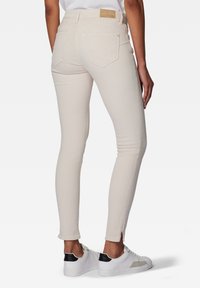 Jean beige skinny en denim, avec une coupe slim, deux poches arrière, et une petite fente à l'ourlet, porté avec des baskets blanches.