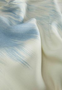 Lättviktig tyg med en mjuk textur, med ett blått och vitt abstrakt mönster. Designen inkluderar flytande penseldragsliknande märken.