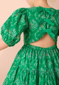 Abito floreale verde con maniche a sbuffo, schiena scoperta con tre dettagli a fiocco e gonna a strati con dettagli di tessuto arricciato.