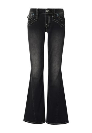 Femme debout face à l'avant, portant un t-shirt noir court avec un petit logo et un jean bootcut foncé délavé avec des baskets blanches.