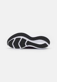 Semelle en caoutchouc noir avec un motif de grip texturé, une forme courbée et des accents blancs contrastants le long des bords.