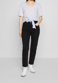 Camiseta gris claro de cuello en V y mangas cortas, suéter azul anudado a la cintura, combinado con jeans negros y zapatillas altas blancas.