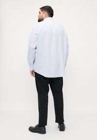 Jasnoniebieska, luźna koszula z długim rękawem i karczkiem z tyłu. Całość uzupełniają czarne spodnie oraz czarne sznurowane buty.