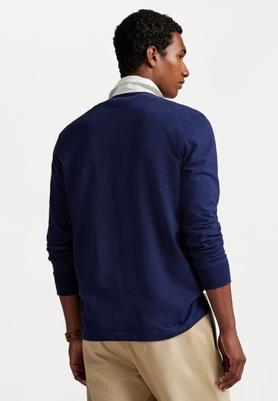 Navyblauw langemouwen shirt van katoen. Heeft een ronde halslijn en ribbelmanchetten. Model draagt een beige broek.