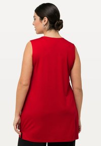Červený bezrukávový top z jemné tkaniny, s kulatým výstřihem a bočními rozparky na spodním okraji pro snadný pohyb.