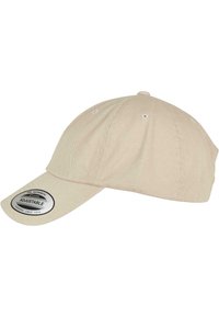 Gorra de béisbol ajustable color beige con visera curva, hecha de algodón, seis orificios de ventilación y una llamativa etiqueta negra en la parte frontal.