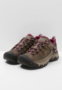 Braune Wanderschuhe mit einer strukturierten Oberseite, pinken Akzenten und strapazierfähigen Gummisohlen. Mit Schnürsenkeln und einer verstärkten Zehenkappe.