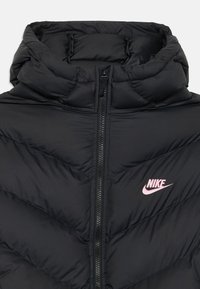 Casaco puffer preto com colarinho alto, fecho de correr e costura em chevron. Logótipo da Nike em rosa notável no peito esquerdo. Material suave.