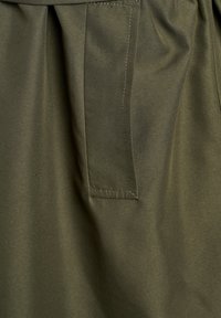 Olijfgroen stof met een gladde textuur. Bevat een zijzak en plooidetails, met contrasterende stiksels langs de naden.