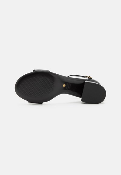 Sandale à talons hauts noire avec une tige en cuir lisse, détail de boucle et une semelle en caoutchouc texturé pour l'adhérence.