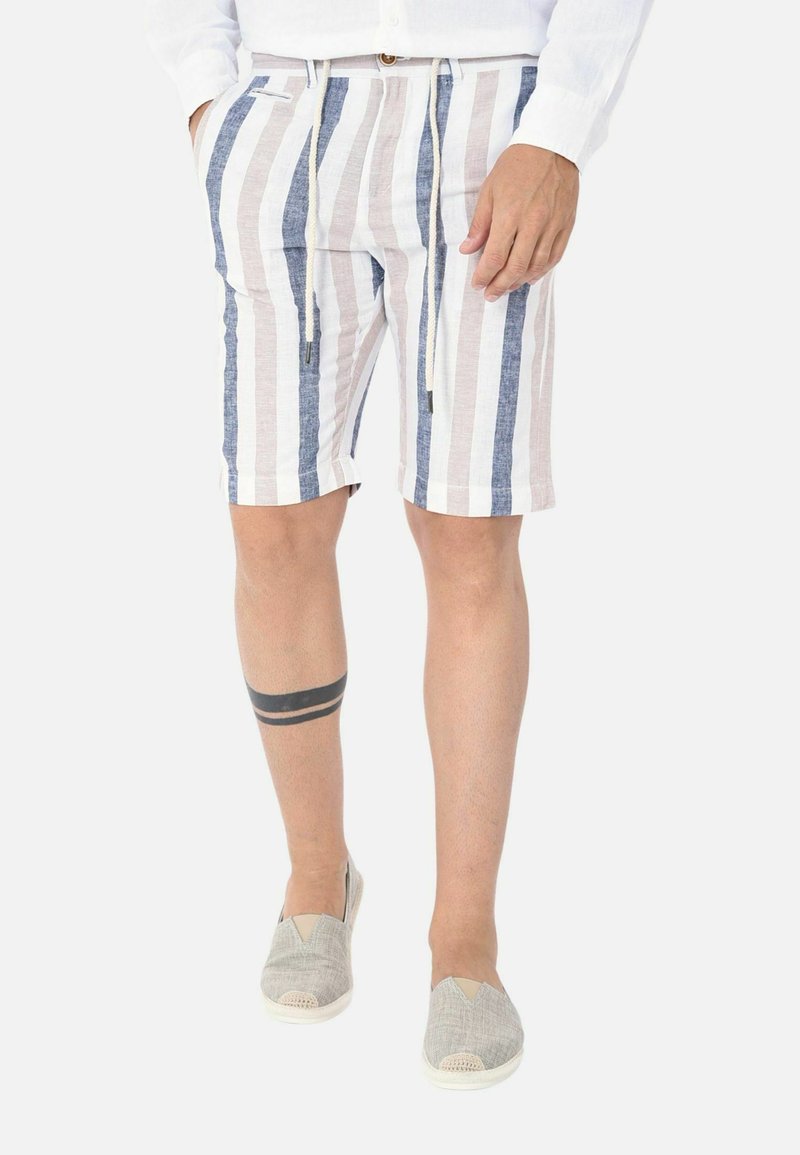 Bermuda in lino a righe con strisce verticali blu e beige, dotate di vita elastica e coulisse. Indossate con scarpe slip-on grigie.