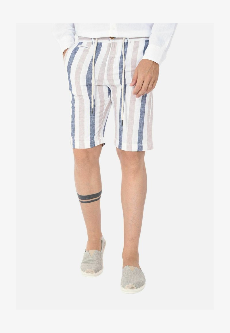 Bermuda in lino a righe con strisce verticali blu e beige, dotate di vita elastica e coulisse. Indossate con scarpe slip-on grigie.