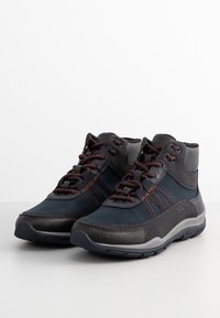 Zapatillas altas que combinan textil azul oscuro y ante gris, con pespuntes en marrón y diseño con cordones para un ajuste seguro.