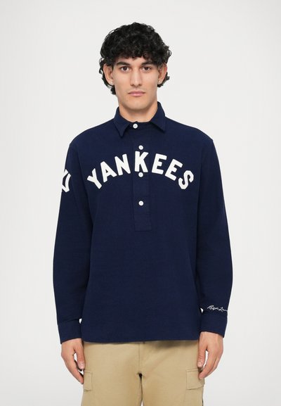 Cămașă din stofă închisă, cu mânecă lungă, cu text alb "Yankees" pe piept, guler cu nasturi și detalii la manșete.