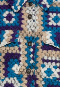 Knoop-up jas met een textuurstof en een geometrisch patroon in blauw, paars, wit en beige, aangevuld met donkere knopen.