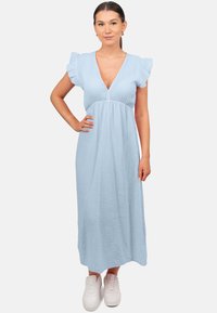 Lichtblauwe maxi-jurk van textuurstof, met een V-hals, gerimpelde korte mouwen en een losse pasvorm. Draagt met witte sneakers.