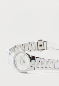 Montre-bracelet en métal argenté avec un boîtier octagonal et un cadran blanc. Présente des marquages minimalistes et une finition polie avec une couronne texturée.