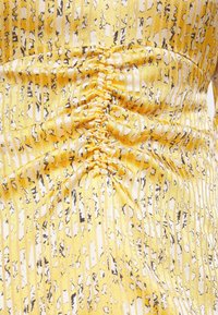 Gult tyg med ett upprepande mönster av vita och svarta vertikala ränder. Rynkade detaljer i mitten skapar textur och form.