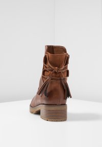 Botte de cheville en cuir marron avec un talon plat, ornée de pampilles à l'arrière et d'une texture lisse. Fermeture zippée sur le côté, semelle robuste.