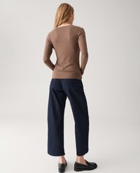 Woman standing facing away wearing a brown ribbed long-sleeve top, dark wide-leg jeans, and black loafers against a plain background.