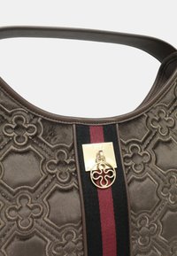 Borsa a mano in velluto marrone con un motivo geometrico, una chiusura in metallo dorato, accenti a strisce rosse e nere e un charm rotondo con logo.