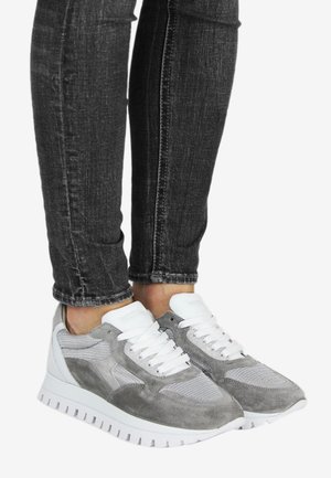 Baskets en daim gris et mesh avec des accents blancs, dotées d'une semelle épaisse et d'un design texturé, portées avec un jean foncé.