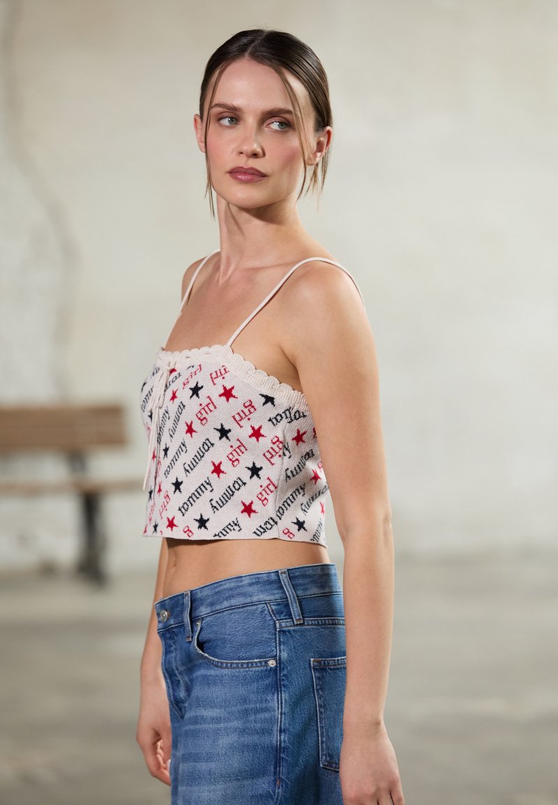 Kuttet tanktopp i hvitt stoff, med rød og svart tekst og stjernemønster. Kombinert med høyt liv blå denimshorts.