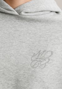 Grijze hoodie van zacht materiaal, met een subtiele lichtgrijze logo op de borst, met een klassiek ontwerp van de capuchon.