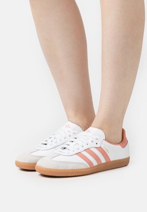 Sneakers bianchi con strisce e dettagli rosa, con una tomaia in pelle scamosciata e pelle, punta tonda e suola in gomma. Design classico con chiusura con lacci.
