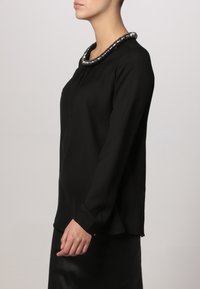Zwarte blouse met lange mouwen, voorzien van een ronde kraag met zilveren kraaldetails, gemaakt van soepel stof, met een loose fit en zijsplitten.