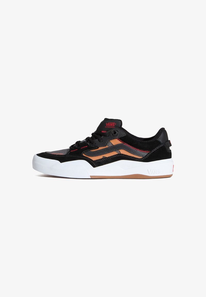 Chaussure de skate Vans basse noire et marron avec semelle en caoutchouc blanche, lacets noirs, détails de couture rouge, et logo Vans sur la languette et la semelle.