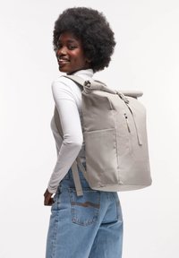 Grå rulltoppsryggsäck med en dragkedjeförsedd framficka, justerbara remmar och en texturerad yta. Lättviktig och funktionell design.