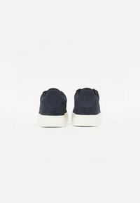 Mørk marineblå semsket sneakers med lav profil, hvite gummisalder og detalj med logo bak. Myk tekstur og minimalistisk design.