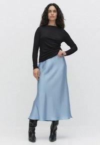 Czarny, teksturowany top z długim rękawem w połączeniu z jasnoniebieską satynową spódnicą midi, charakteryzującą się gładkim wykończeniem. Uzupełniony wysokimi, czarnymi botkami.