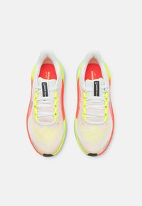 Zapatillas de correr blancas y neón con parte superior de malla, con detalles en rosa y amarillo, suela texturizada y sistema de cordones estándar.