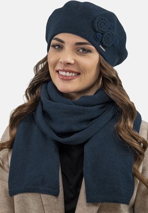 Sada navy modré vlněné baret a šála. Baret má tři látkové růžičky; obě položky mají měkký, texturovaný povrch.