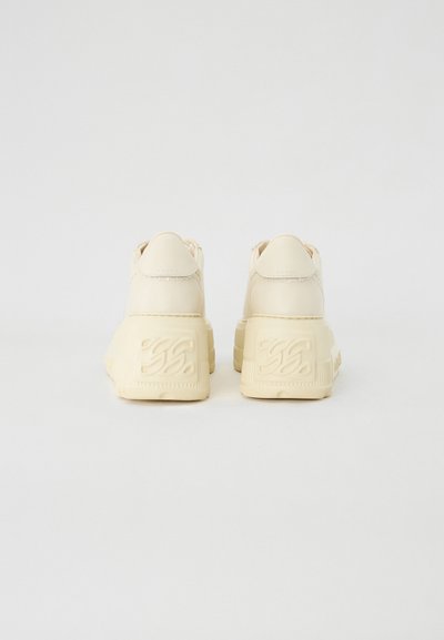Beige platform sneaker, sima bőr külsővel, párnázott nyakkal és texturált gumitalppal, amelyen a saroknál dombornyomott márkajelzés található.