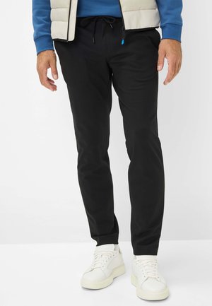 Zwarte taps toelopende broek van een lichtgewicht stof, met een trekkoord in de taille en zijzakken, gedragen met witte sneakers.
